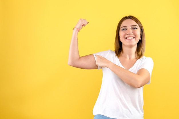 Front view of young woman flexing on yellow wall