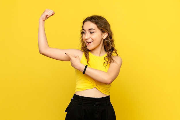 Free photo front view of young woman flexing on yellow wall