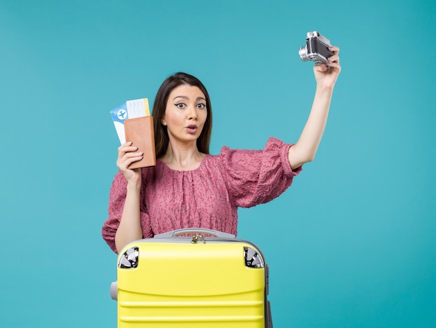 Вид спереди молодая женщина собирается в отпуск, держа камеру с фото на синем фоне путешествие отпуск женщина за границу море
