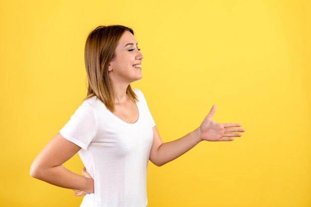 Front view of young woman greeting someone on yellow wall