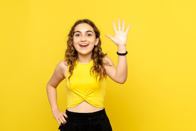 Front view of young woman greeting on yellow wall