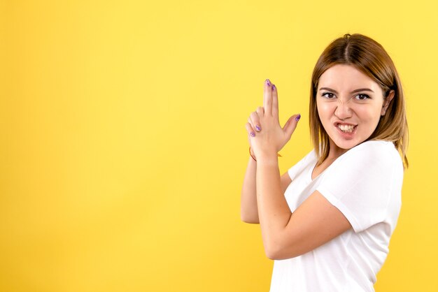 Front view of young woman in gun holding pose on yellow wall