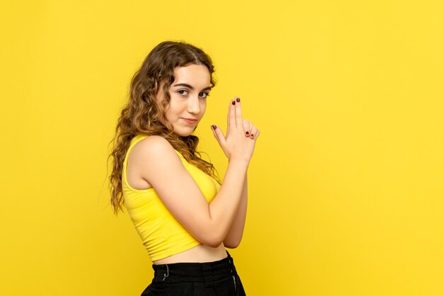 Front view of young woman in gun holding pose on yellow wall