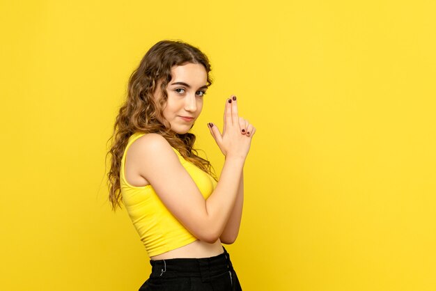 Вид спереди молодой женщины в позе, держащей пистолет на желтой стене