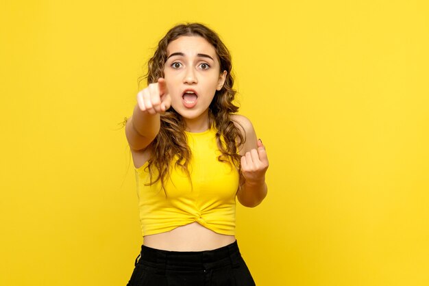 Front view of young woman happily pointing on yellow wall