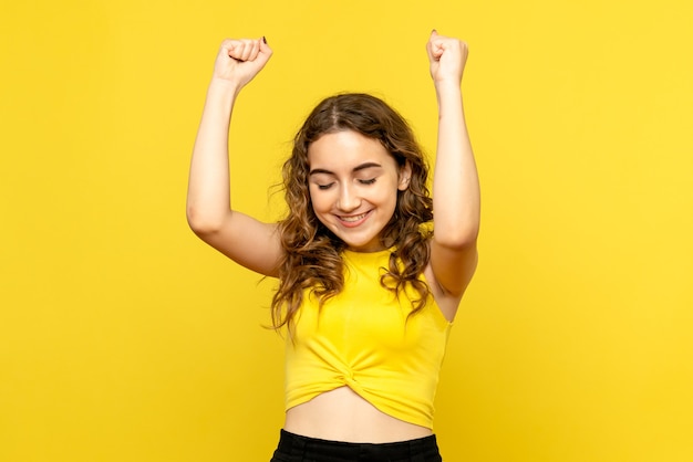 Front view of young woman happily rejoicing on a yellow wall