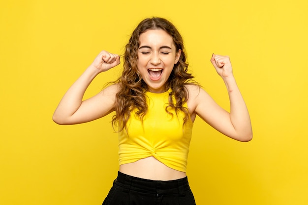 Front view of young woman happily rejoicing on yellow wall