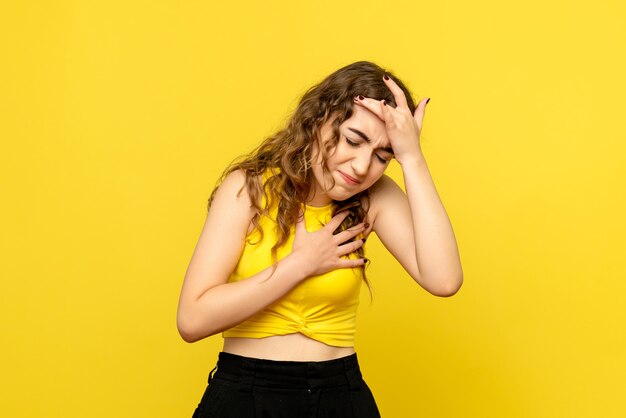 Front view of young woman having headache on yellow wall