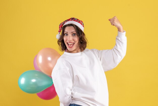 Front view young woman hiding colorful balloons on yellow desk new year christmas color holiday woman emotion