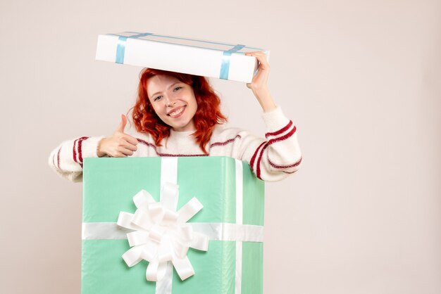 クリスマスプレゼントの中に隠れて白い壁に笑みを浮かべて若い女性の正面図