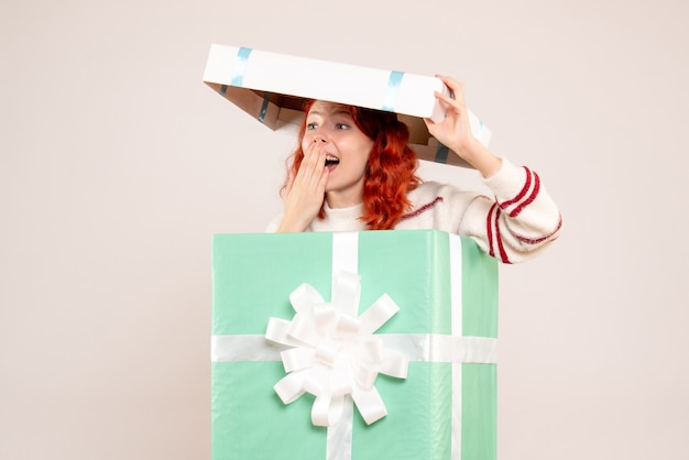 Vista frontale della giovane donna che si nasconde all'interno del regalo di natale sul muro bianco