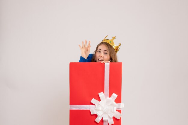 Front view of young woman hiding inside present box on a white wall