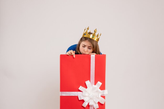 Front view of young woman hiding inside present box on white wall