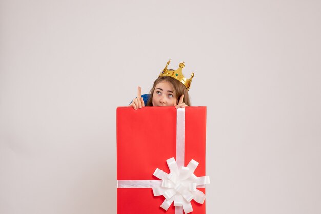 白い壁のプレゼントボックスの中に隠れている若い女性の正面図