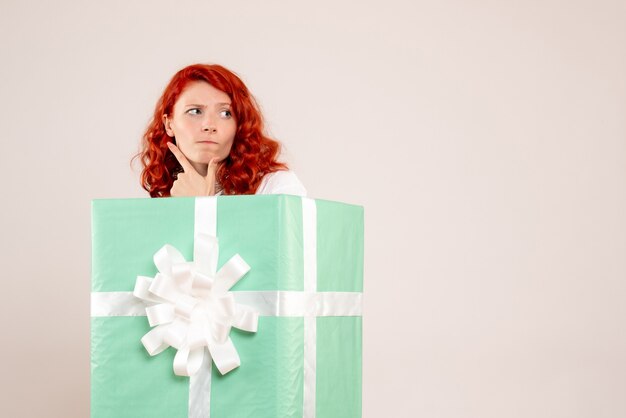 Front view of young woman hiding inside present on a white wall