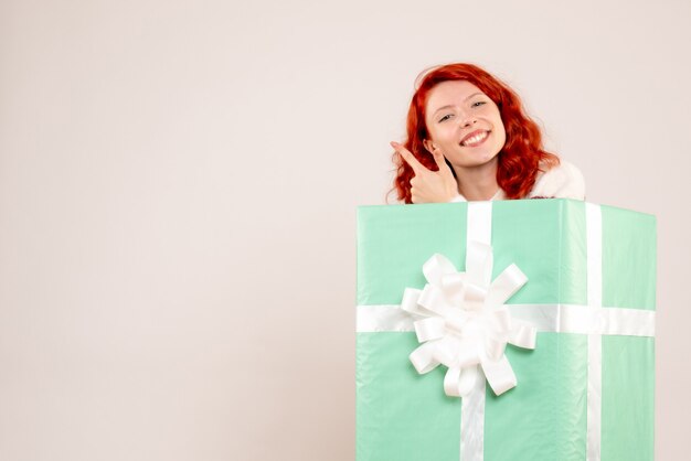 白い壁にプレゼントの中に隠れている若い女性の正面図