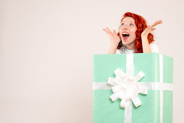 Front view of young woman hiding inside present on the white wall