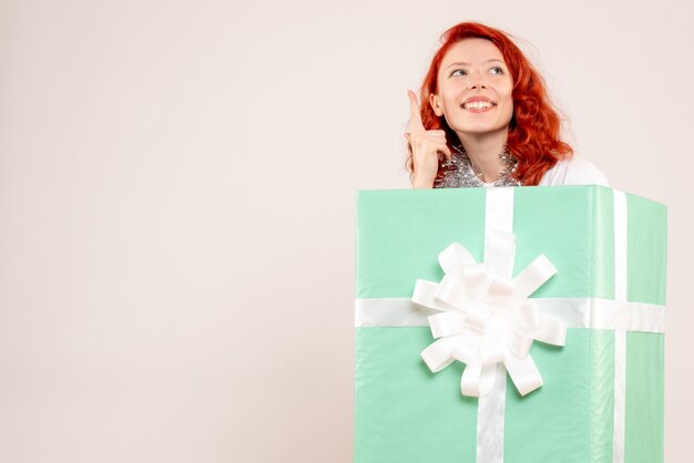 Front view of young woman hiding inside present on white wall