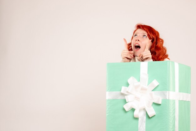 Front view of young woman hiding inside present on white wall