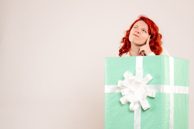 Front view of young woman hiding inside present on white wall