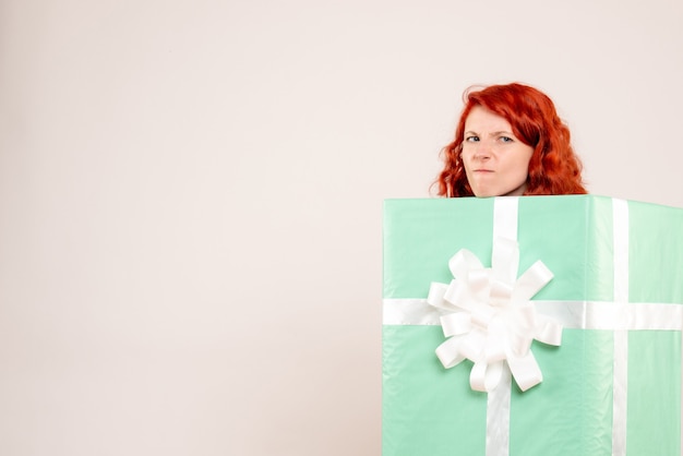 白い壁にプレゼントの中に隠れている若い女性の正面図