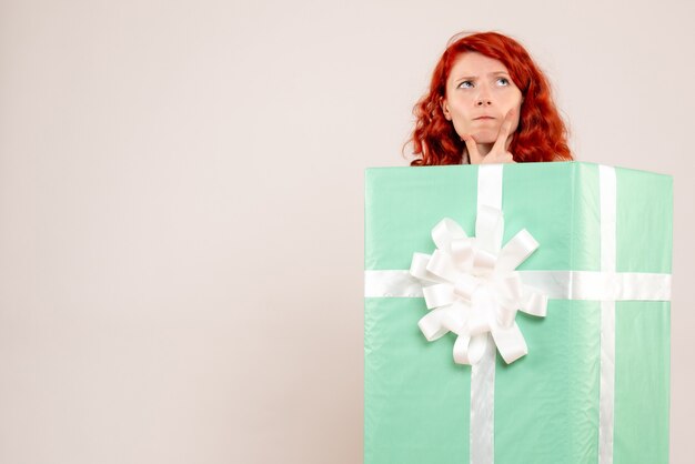 Front view of young woman hiding inside present on white wall