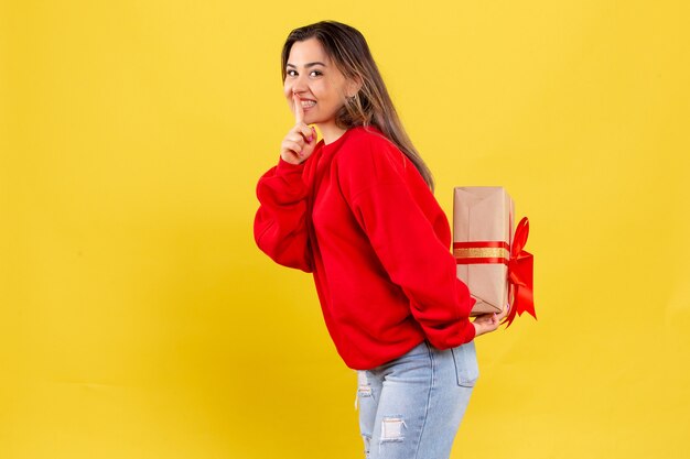 Front view young woman hiding xmas gift behind her back on yellow background