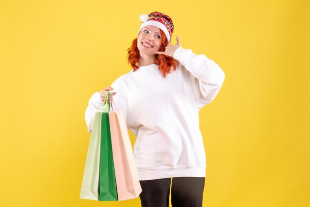 Front view of young woman holding bags from shopping on yellow wall