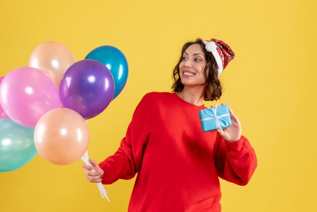 Front view young woman holding balloons and little present on yellow christmas holiday new year emotions color woman