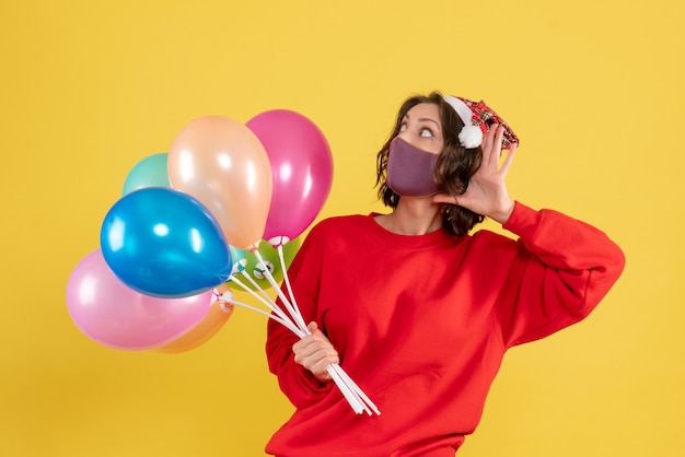 Free photo front view young woman holding balloons in mask listening on yellow celebration party emotion new year color woman