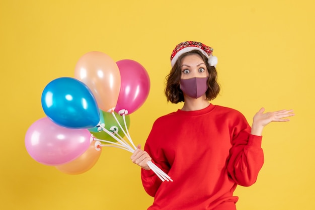 Free photo front view young woman holding balloons in mask on a yellow party new year color celebration emotion woman