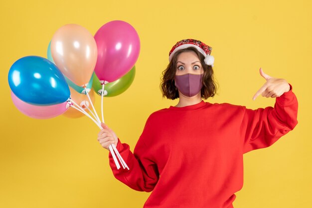 Front view young woman holding balloons in mask on yellow