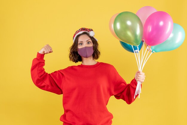 Front view young woman holding balloons in sterile mask on yellow