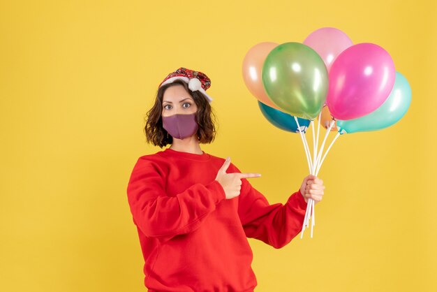 Front view young woman holding balloons in sterile mask on yellow