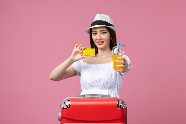 Front view young woman holding bank card and cocktail on pink wall summer voyage trip heat color vacation