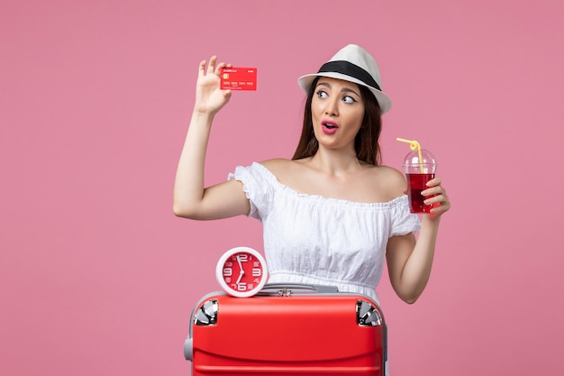 Front view young woman holding bank card and juice on vacation on pink wall voyage color trip summer vacation woman