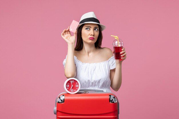 Front view young woman holding bank card and juice on vacation on pink wall voyage trip summer woman