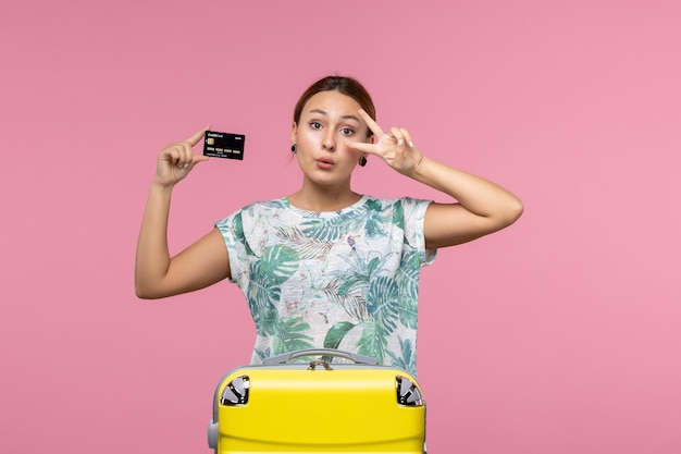 Front view of young woman holding bank card on the light-pink wall