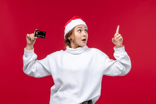 Вид спереди молодая женщина, держащая банковскую карту на светло-красном фоне