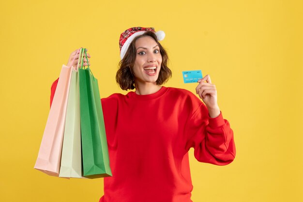 Front view young woman holding bank card and packages on yellow