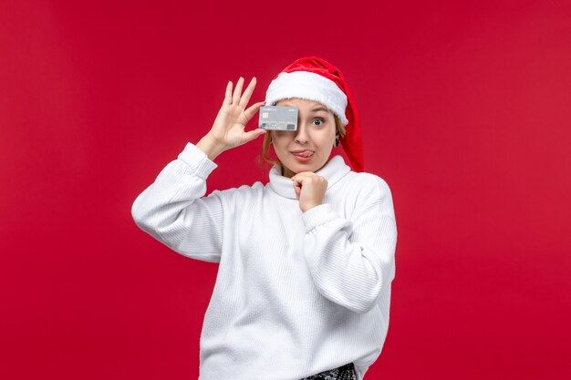 Front view young woman holding bank card on red desk