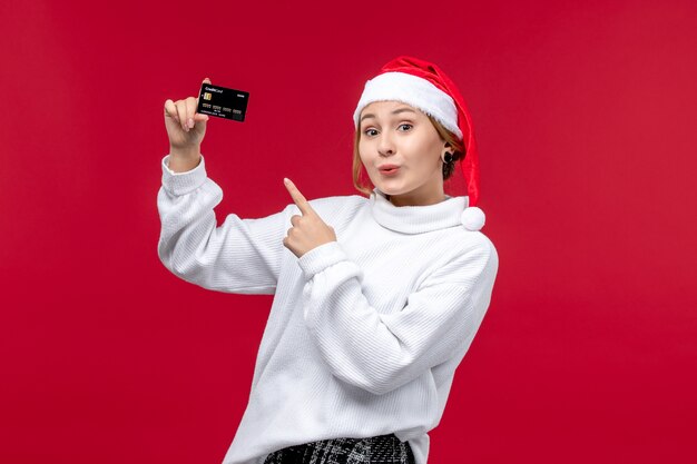 Front view young woman holding bank card on red desk