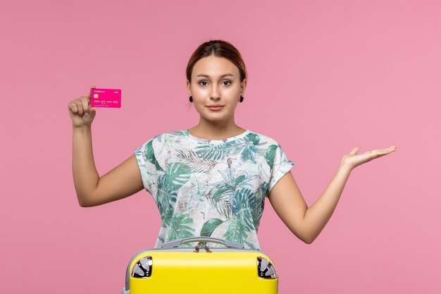 Front view young woman holding bank card on vacation on pink floor summer rest color voyage vacation woman