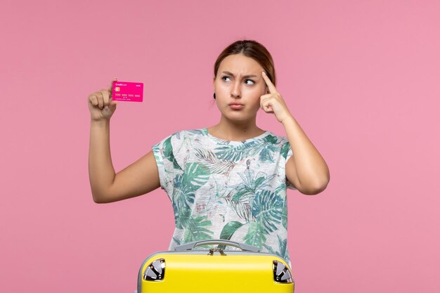 Front view young woman holding bank card on vacation on a pink wall summer rest voyage vacation woman