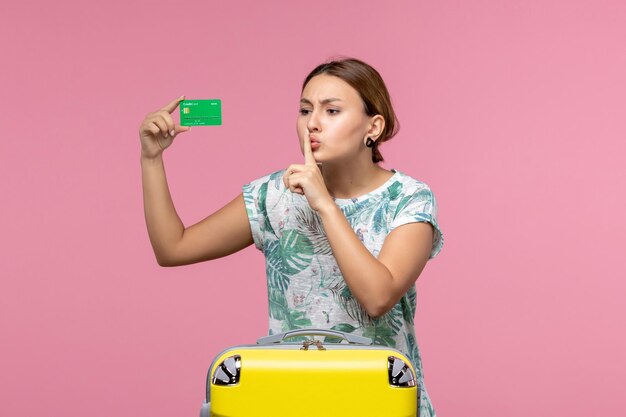 ピンクの壁の夏の航海旅行休息の女性の休暇で休暇中に銀行カードを保持している正面図若い女性