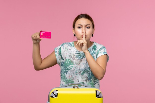 Front view young woman holding bank card on vacation on pink wall voyage summer vacation woman rest