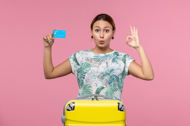 淡いピンクの壁の休憩飛行航海飛行機の女性に黄色の休暇バッグと銀行カードを保持している正面図若い女性