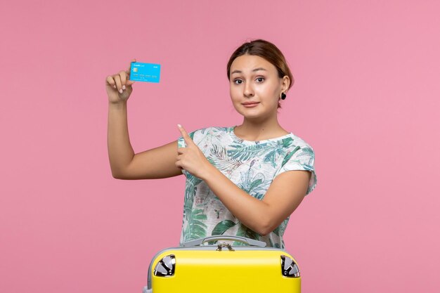ピンクの壁の休憩飛行航海飛行機の女性に黄色の休暇バッグと銀行カードを保持している正面図若い女性