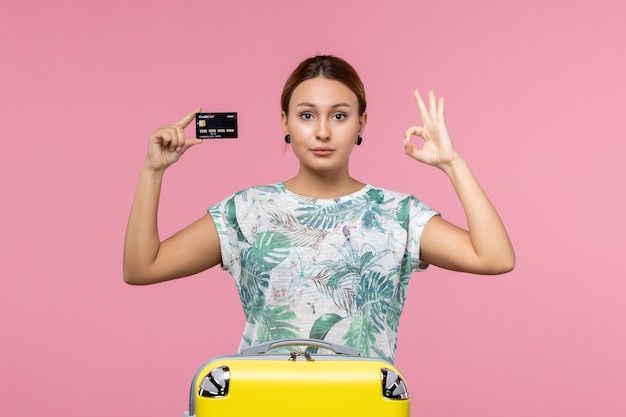 Front view of young woman holding black bank card on light pink wall