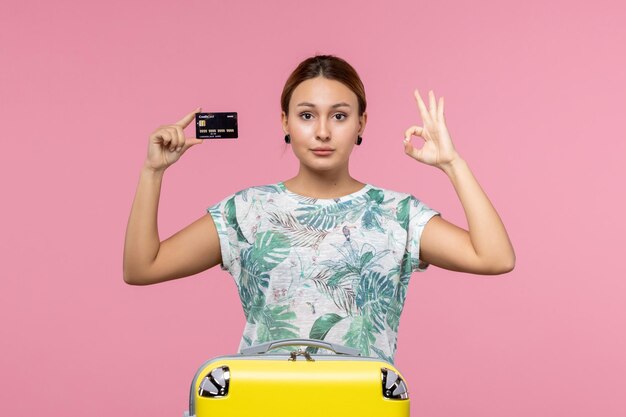 Вид спереди молодой женщины, держащей черную банковскую карту на светло-розовой стене
